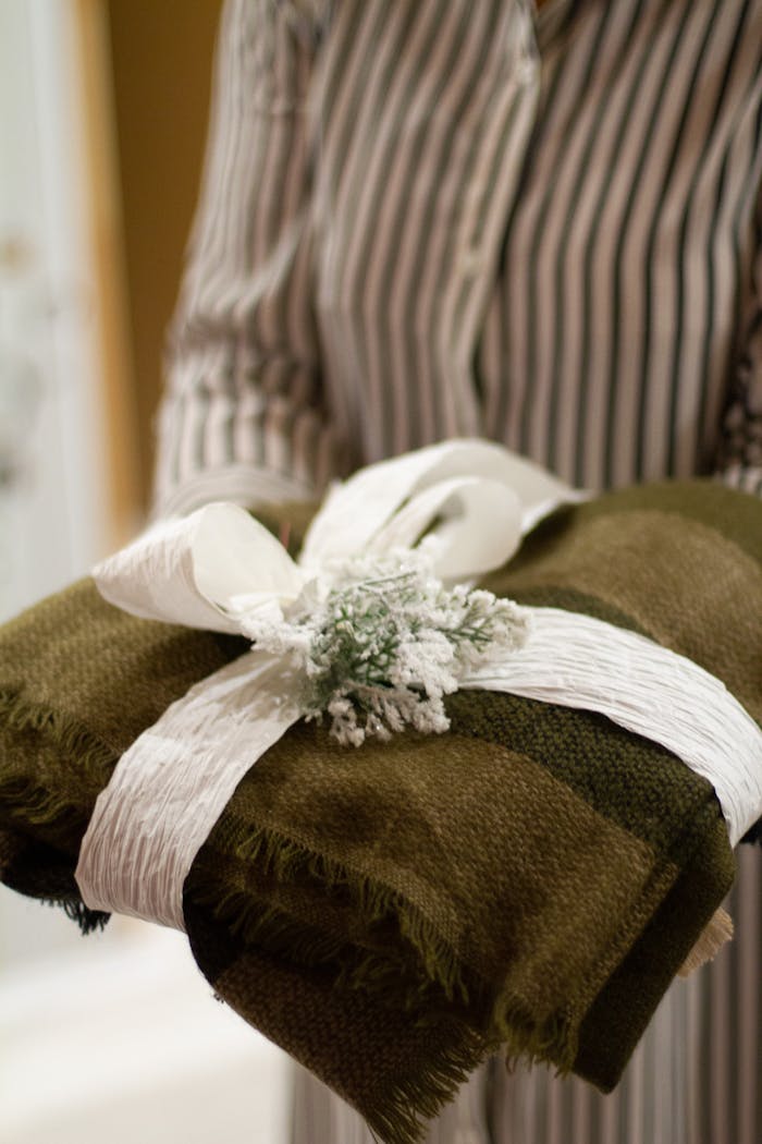 A close-up of a green textile gift wrapped with a decorative white ribbon in someone's hands.