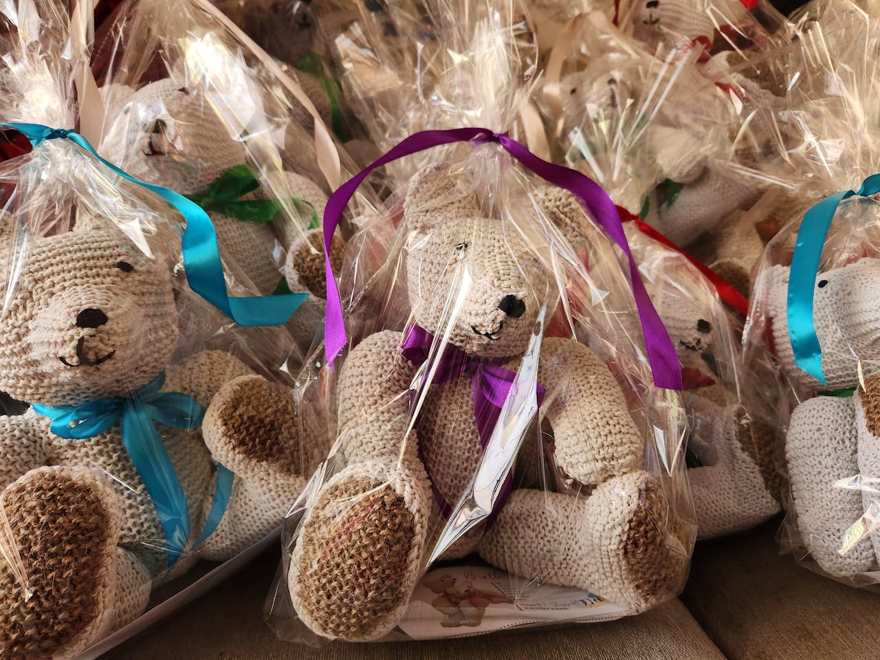 Adorable handmade crochet teddy bears wrapped in cellophane with colorful ribbons, perfect for gifts.